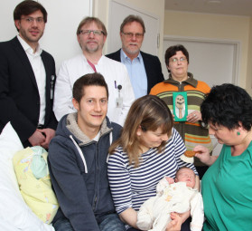 Bürste im Einsatz: Die leitende Hebamme des Asklepios Klinikums Schwalmstadt, Ramona Naumann (rechts) bürstet Tim Felix Hoos die Haare. Dessen Mutter Alexandra Horst und Vater Marco Hoos freuen sich über das Geschenk des Klinikums. Ebenso Klinikmanager Marco Globes, der Chefarzt der Frauenklinik Dr. Heinz-Josef Kaum, der Abteilungsleiter der Hephata-WfbM Detlef Schwierzeck und Michaela Steinhoff-Damisch, die die Babybürsten fertigt (hinten v.l.). Foto: nh hephata140212