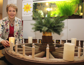 Inge Wickert macht eine Kerze am Adventskranz an. Foto: nh adventskranz-hephata141203