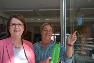 Ministerin Priska Hinz (li.) gemeinsam mit Aria van Dijk, Beraterin der Verbraucherzentrale, beim Anbringen des Refill-Aufklebers an der Verbraucherzentrale in Wiesbaden. Foto: Umweltministerium