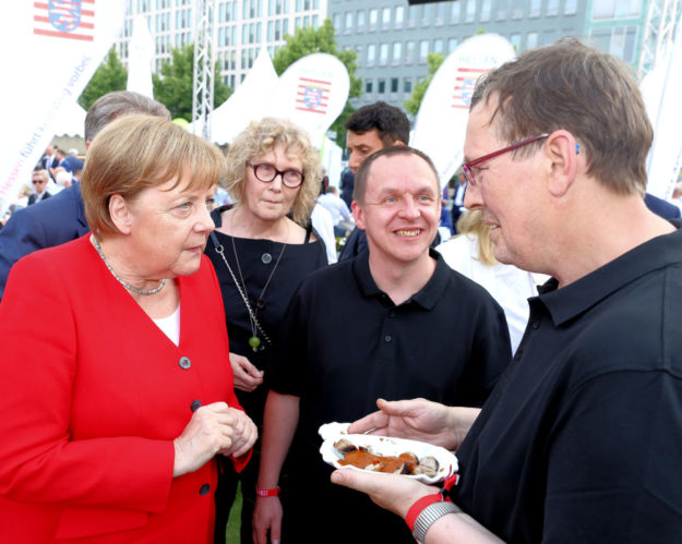Klaus Vogt und Sven Metzner (v.re.) servieren Bundeskanzlerin Angela Merkel beim Hessenfest in Berlin eine »Für Uns«-Currywurst aus der Hephata-Metzgerei Alsfelder Biofleisch. Foto: Hephata