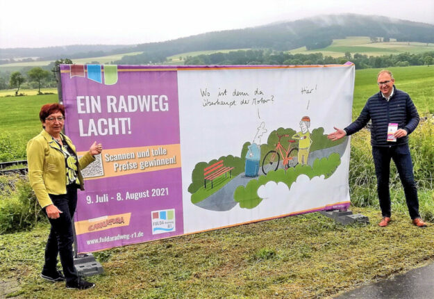 Rotkäppchen-Geschäftsführerin Heidrung Englisch und Niederaulas Bürgermeister Thomas Rohrbach präsentieren einen weiteren Cartoon der langen Ausstellung am Fulda-Radweg R1. Foto: Tourismusservice Rotkäppchenland